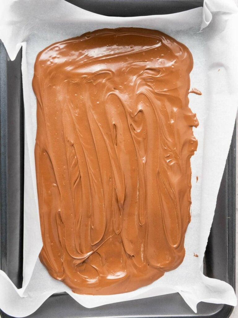 A baking tray lined with parchment paper holds a smooth layer of melted chocolate.