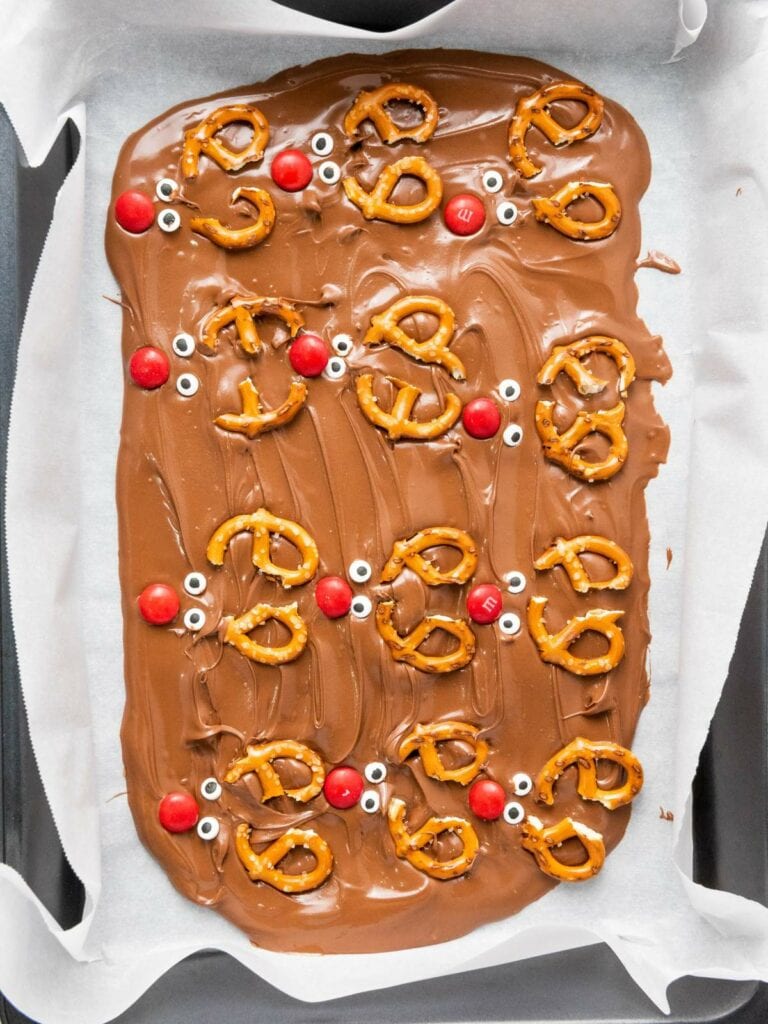 Chocolate bark topped with pretzels, red candies, and candy eyes on parchment paper.