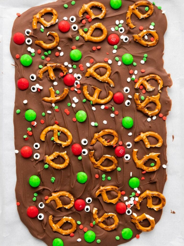 A sheet of chocolate bark topped with pretzels, red and green candy, and festive sprinkles.