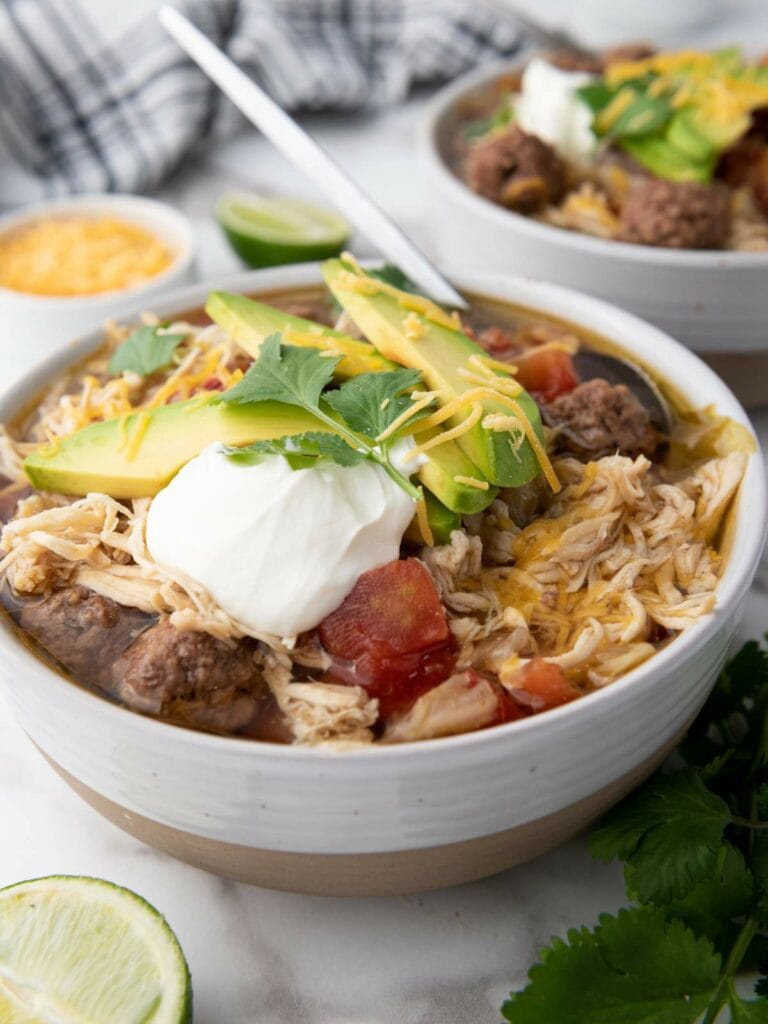 A bowl of taco soup topped with sliced avocado, sour cream, cheese, and cilantro.