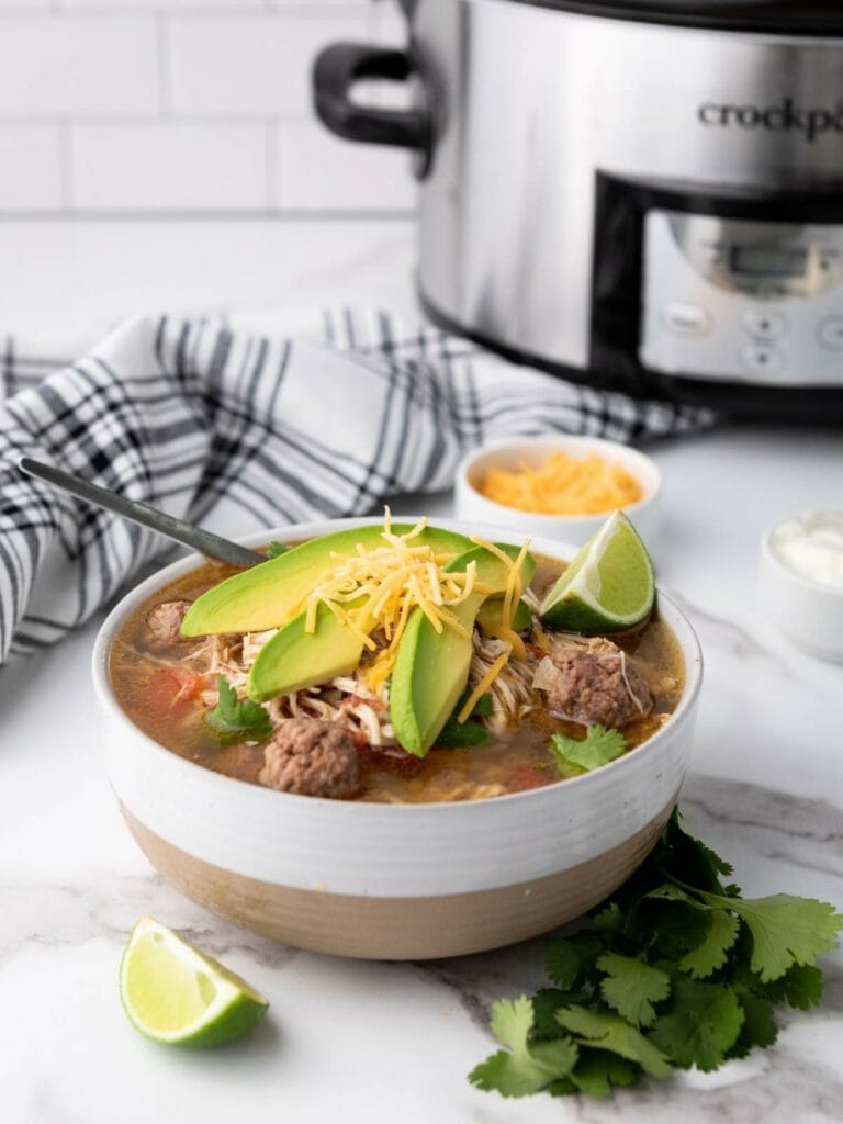 A bowl of taco soup topped with avocado slices, cheese, and herbs.