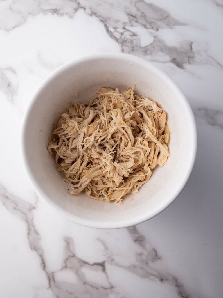 A white bowl filled with shredded chicken on a marble surface.