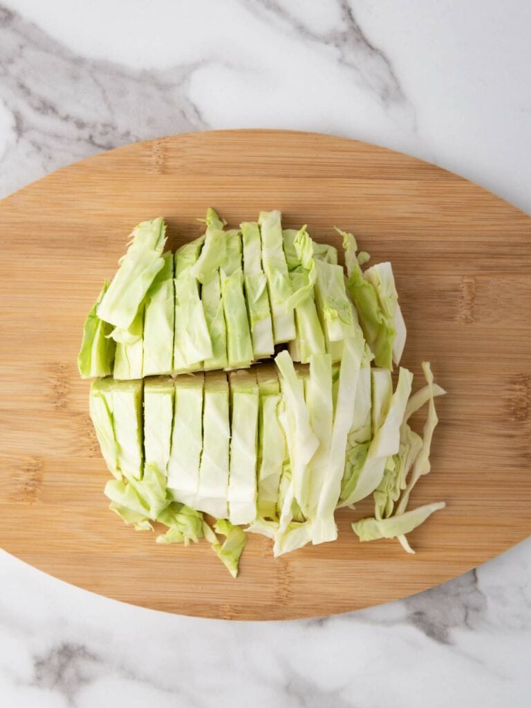 Sliced cabbage arranged on a wooden cutting board on a marble countertop.