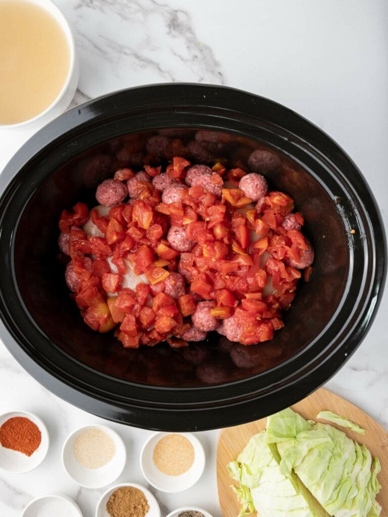 Slow cooker with raw meatballs, chopped tomatoes, and chicken breasts.