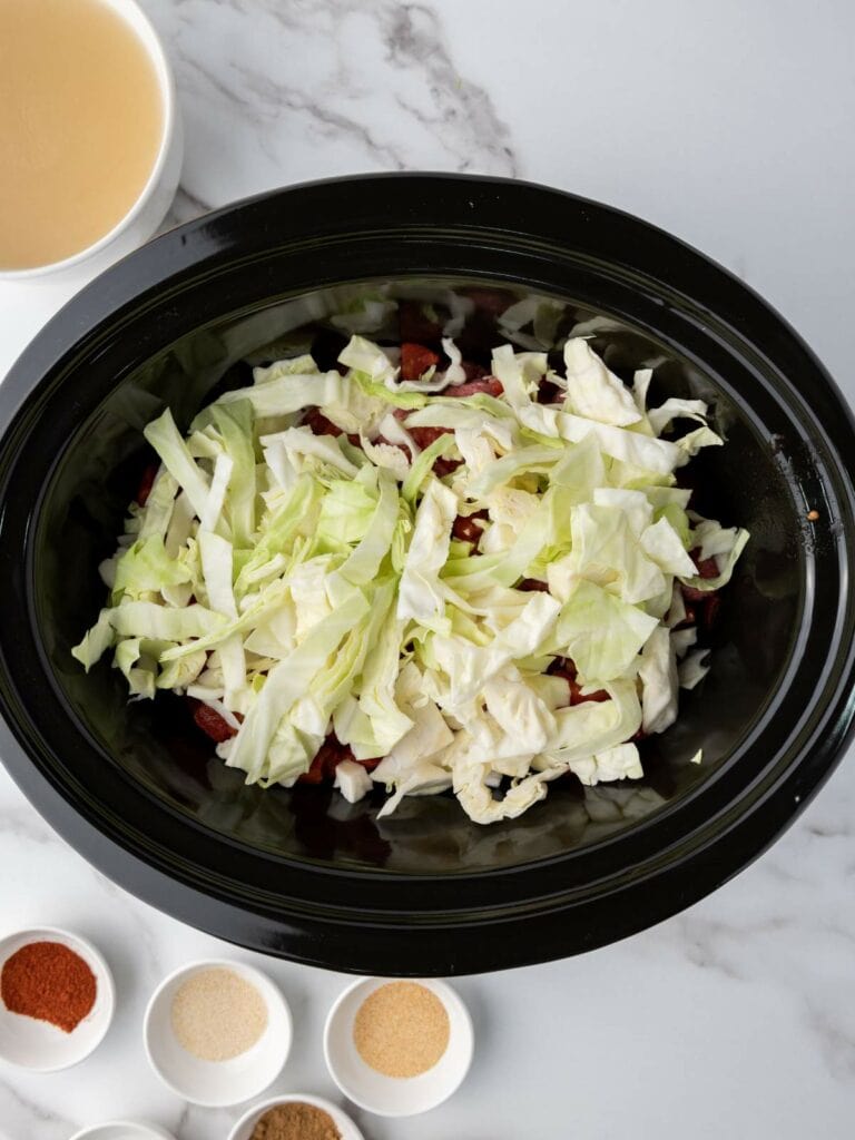 A slow cooker filled with chopped cabbage and meat.