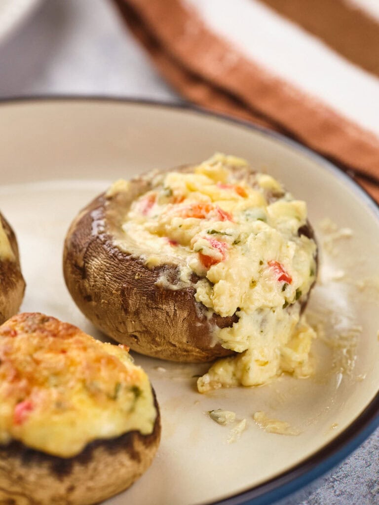 Stuffed mushrooms with a creamy cheese and vegetable filling on a beige plate.