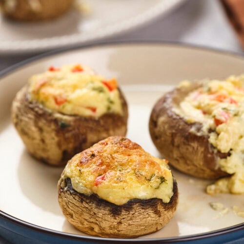 Stuffed mushrooms on a plate, filled with a mixture of cheese and vegetables.