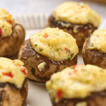 Stuffed mushrooms topped with a cheesy mixture, garnished with herbs and small red pepper pieces.