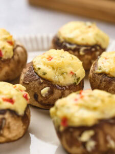 Stuffed mushrooms topped with a cheesy mixture, garnished with herbs and small red pepper pieces.