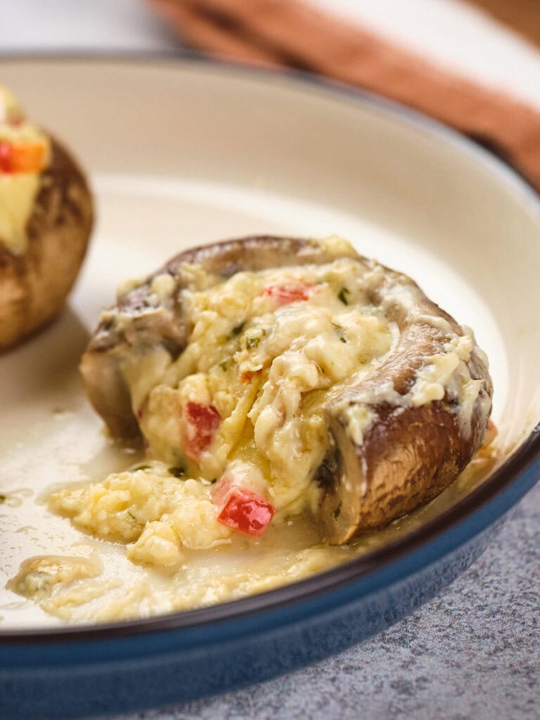 Stuffed mushroom cap with melted cheese and diced vegetables, served on a ceramic plate.