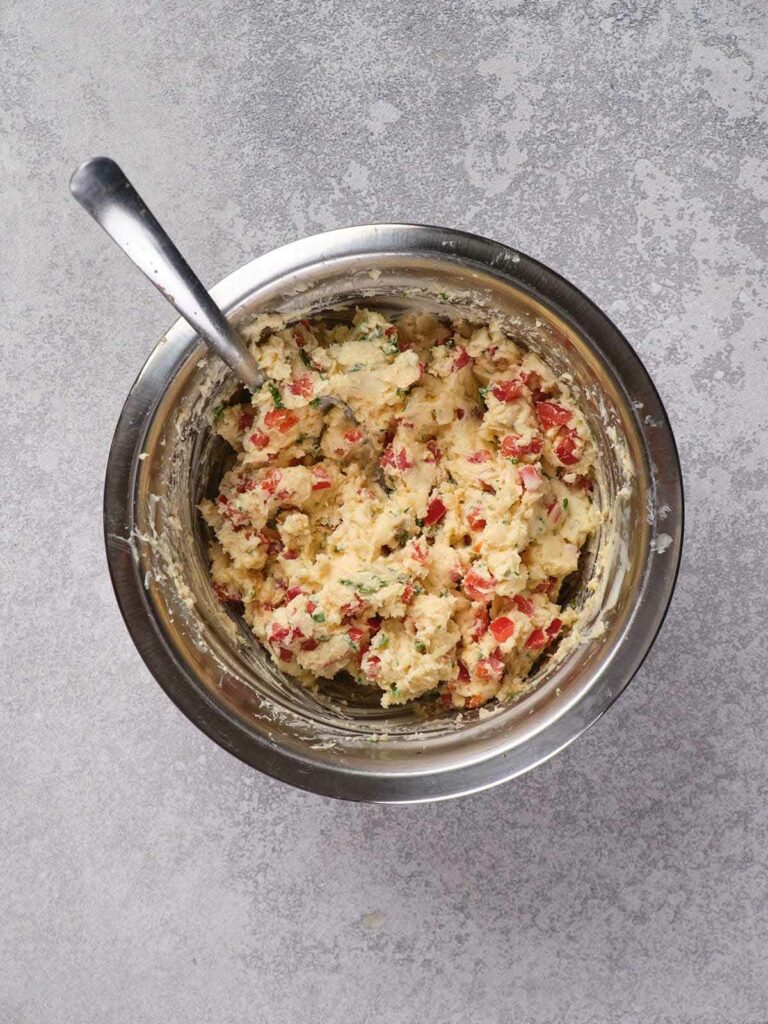 A metal bowl filled with a cream cheese mixture and bright red and green sprinkles,.