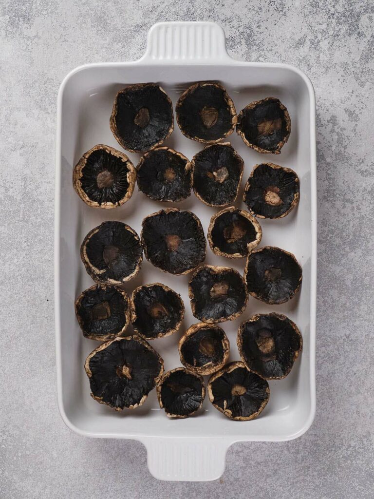 A white baking dish filled with halved portobello mushroom caps on a textured gray surface.