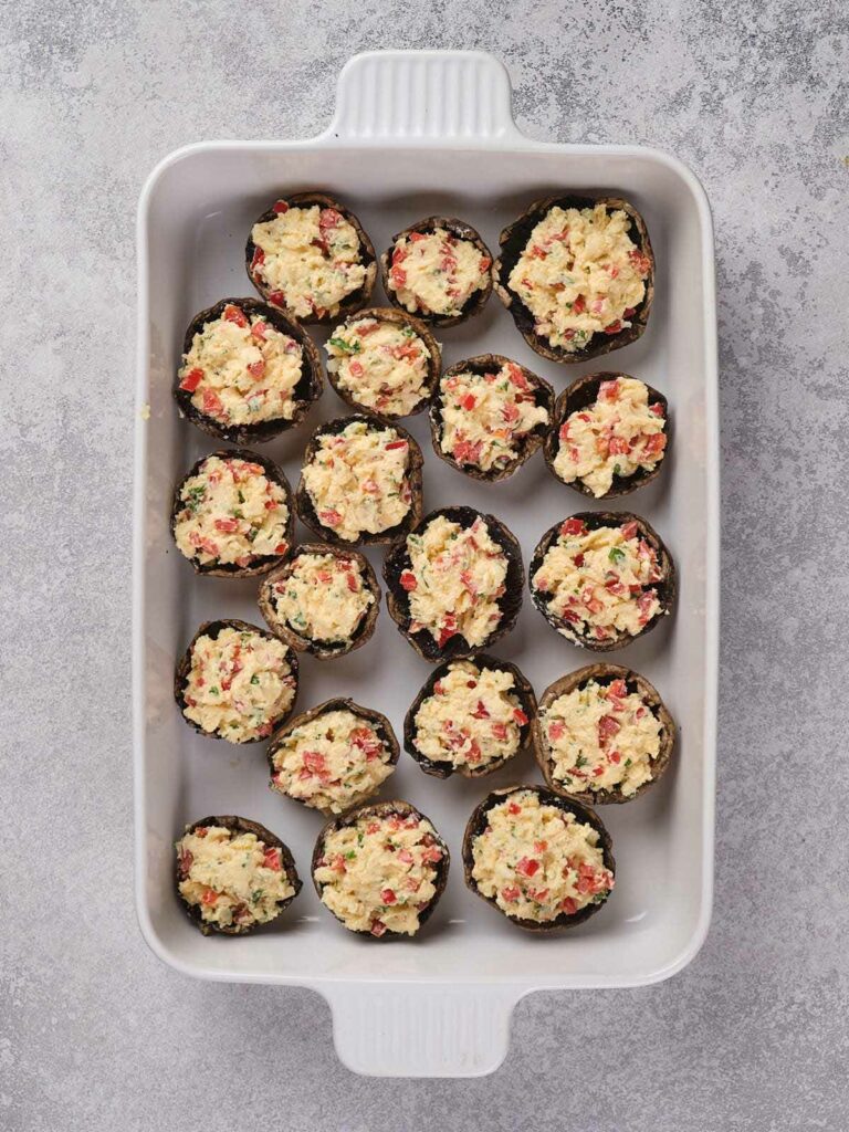 A baking dish filled with stuffed mushroom caps, topped with a mixture of cheese, peppers, and herbs.