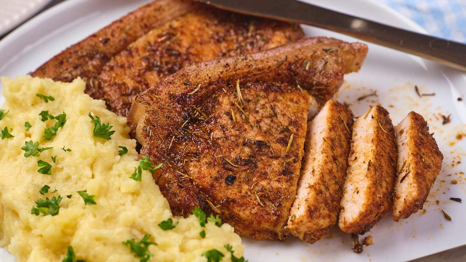 Pork chops seasoned with herbs alongside a serving of mashed potatoes garnished with parsley on a white plate.