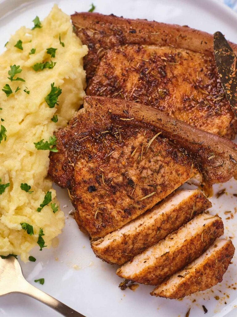 Pork chops with a side of mashed potatoes garnished with chopped parsley on a white plate.