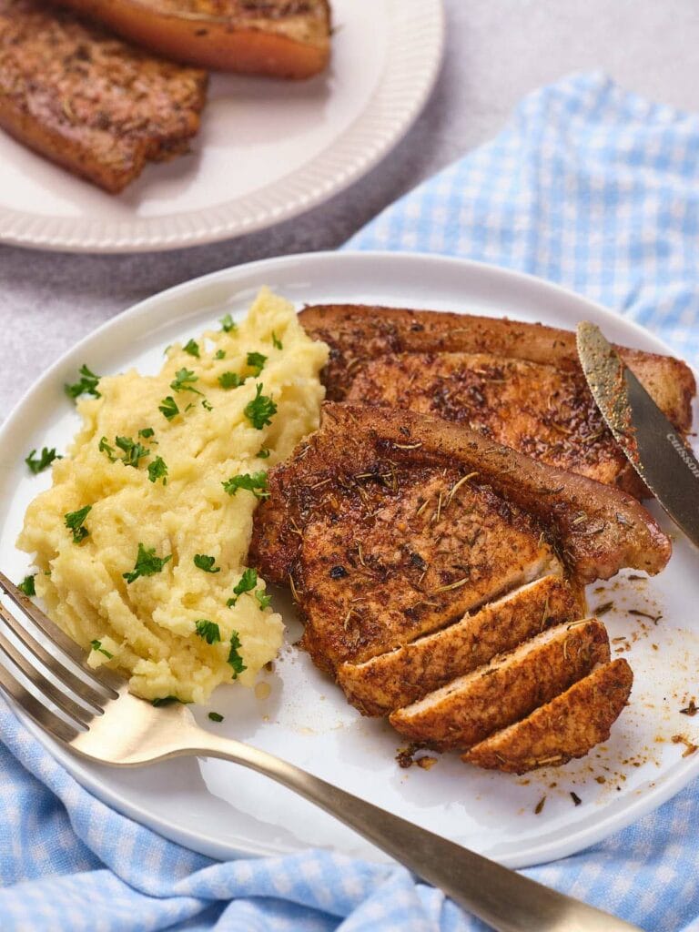 A plate with sliced seasoned pork chops and mashed potatoes, garnished with parsley.