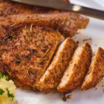 Sliced seasoned pork chops on a plate with a side of mashed potatoes garnished with parsley.