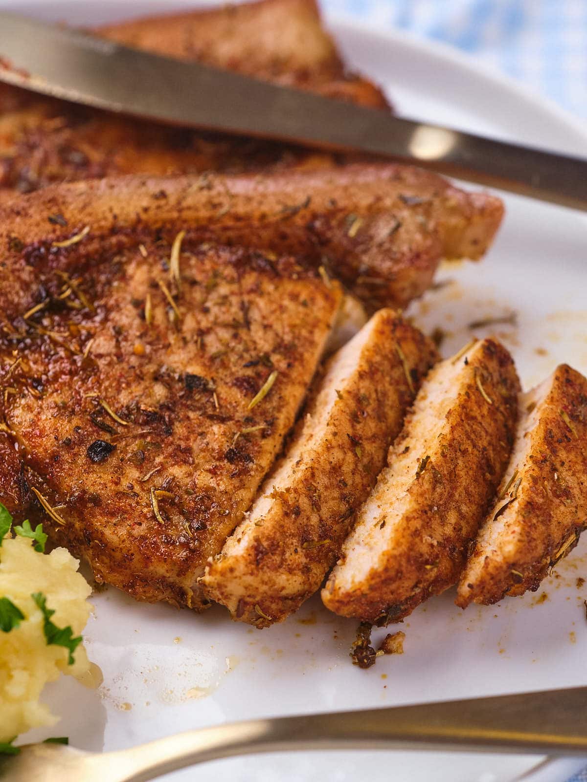 Sliced seasoned pork chops on a plate with a side of mashed potatoes garnished with parsley.