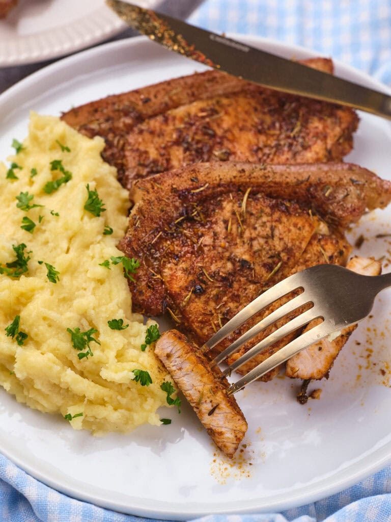 A plate with seasoned grilled pork chops next to a serving of mashed potatoes garnished.