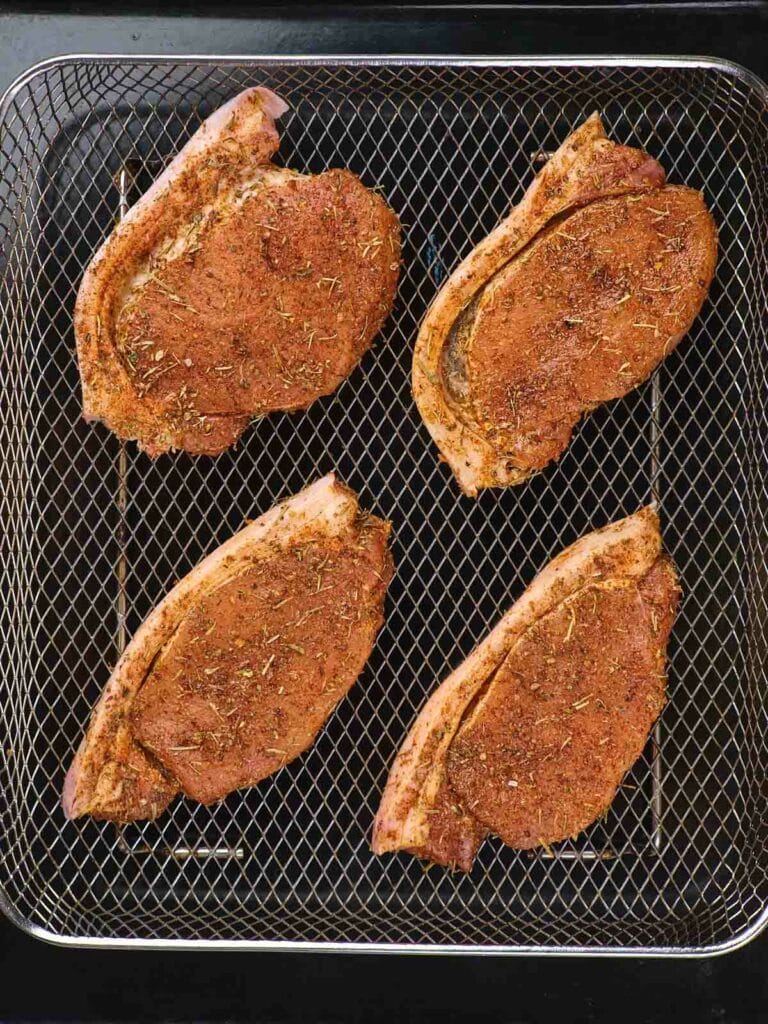 Four seasoned pork chops on a wire rack, ready for cooking.