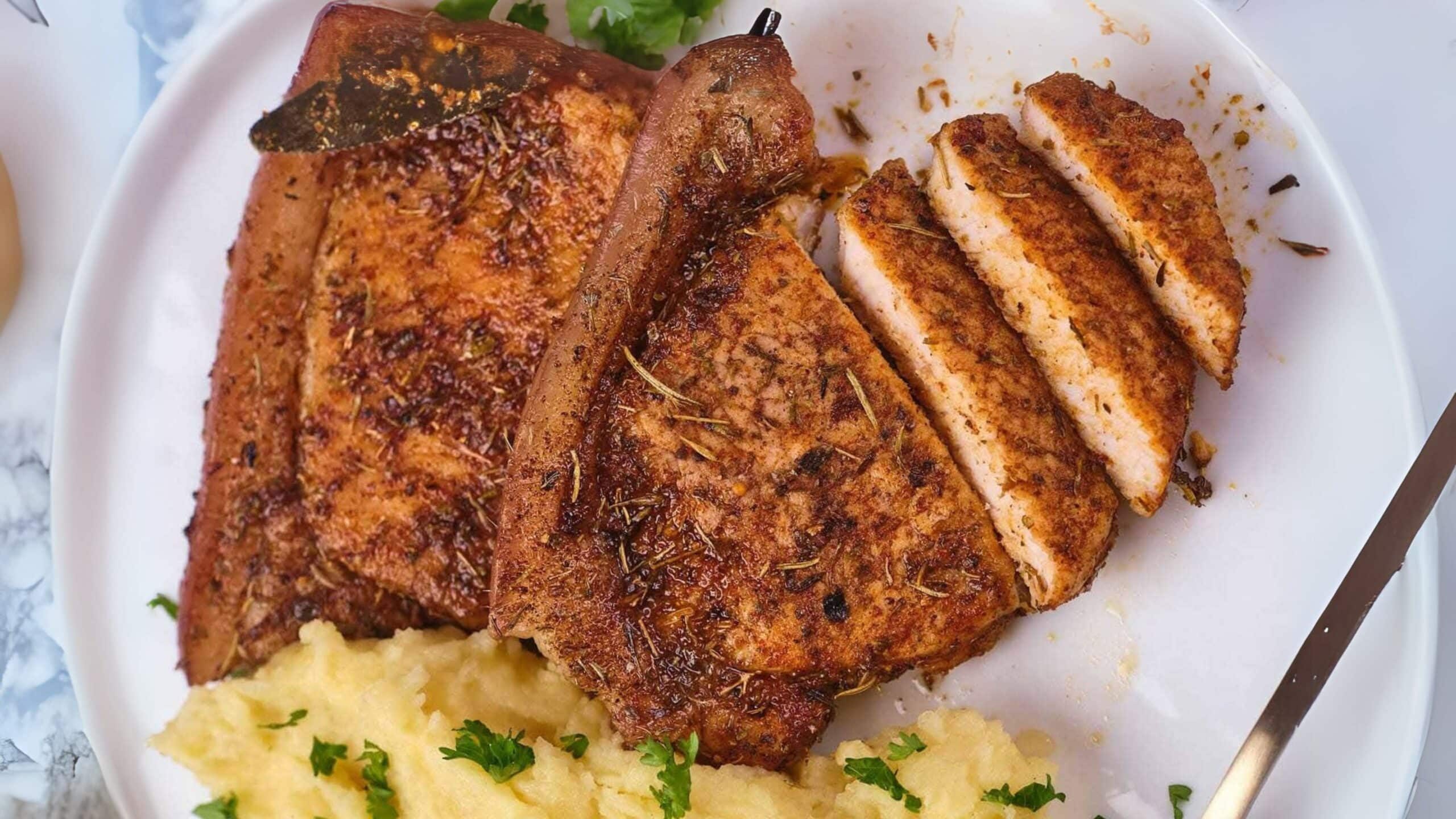 Sliced seasoned pork chop with mashed potatoes garnished with parsley on a white plate.