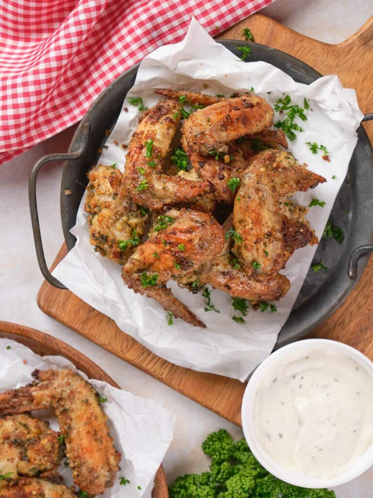 Plate of seasoned baked chicken wings garnished with parsley on a lined tray.