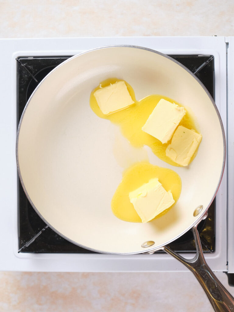 Three pieces of butter melting in a frying pan on a stovetop.