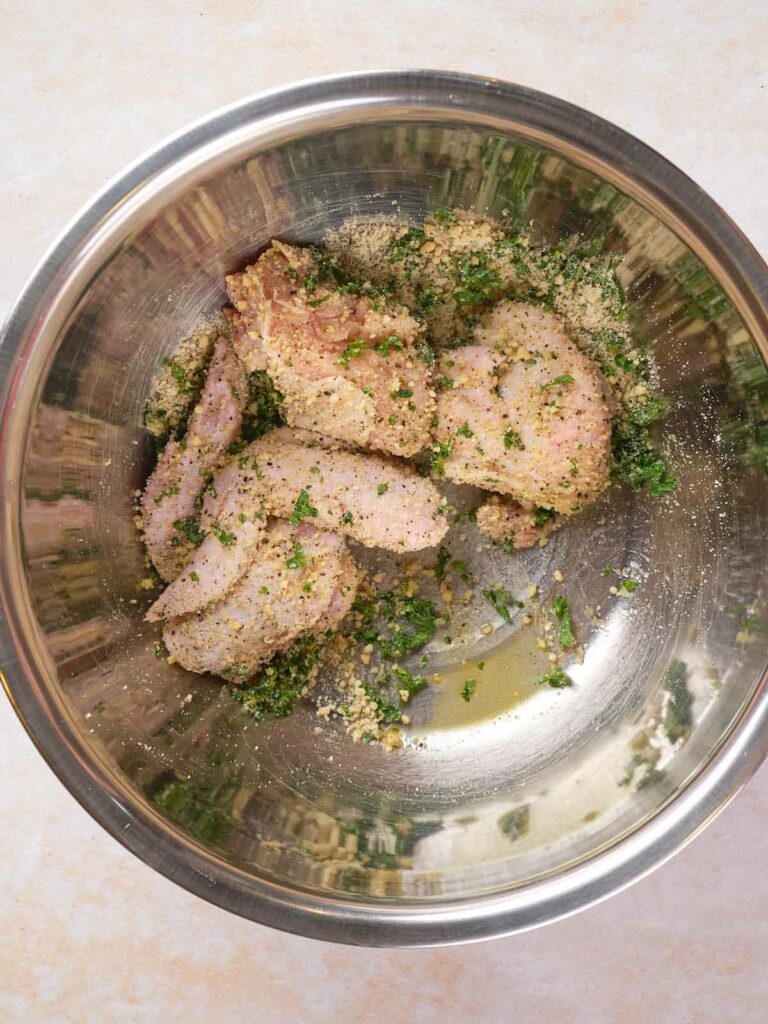 Raw chicken wings coated in bread crumbs, herbs, and spices in a stainless steel mixing bowl.