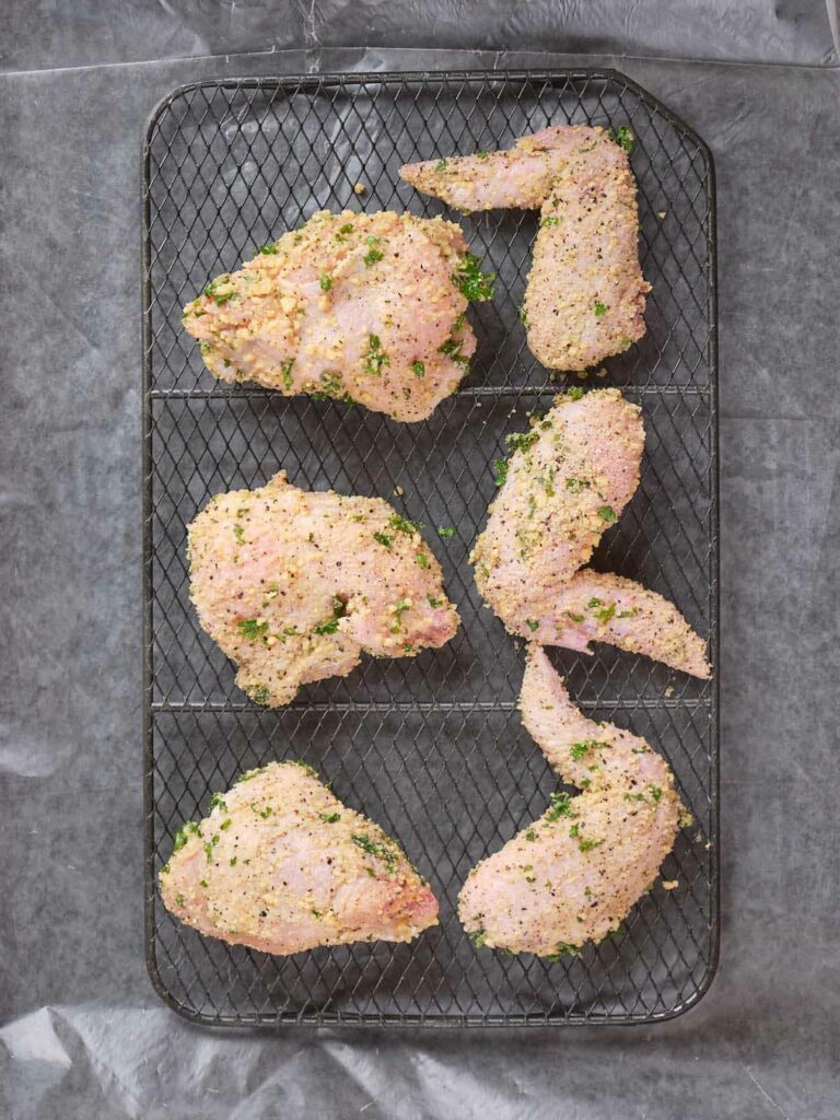 Six raw chicken pieces coated with a crumb mixture, arranged on a wire rack ready for cooking.