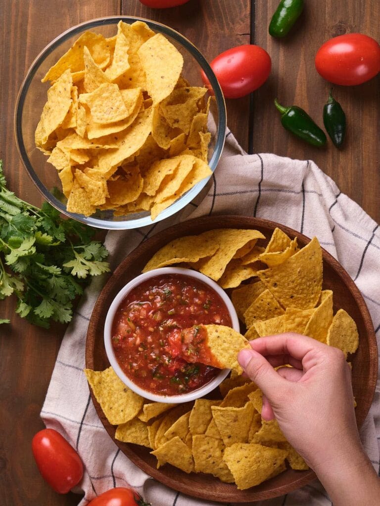 A hand dips a tortilla chip into a bowl of salsa.