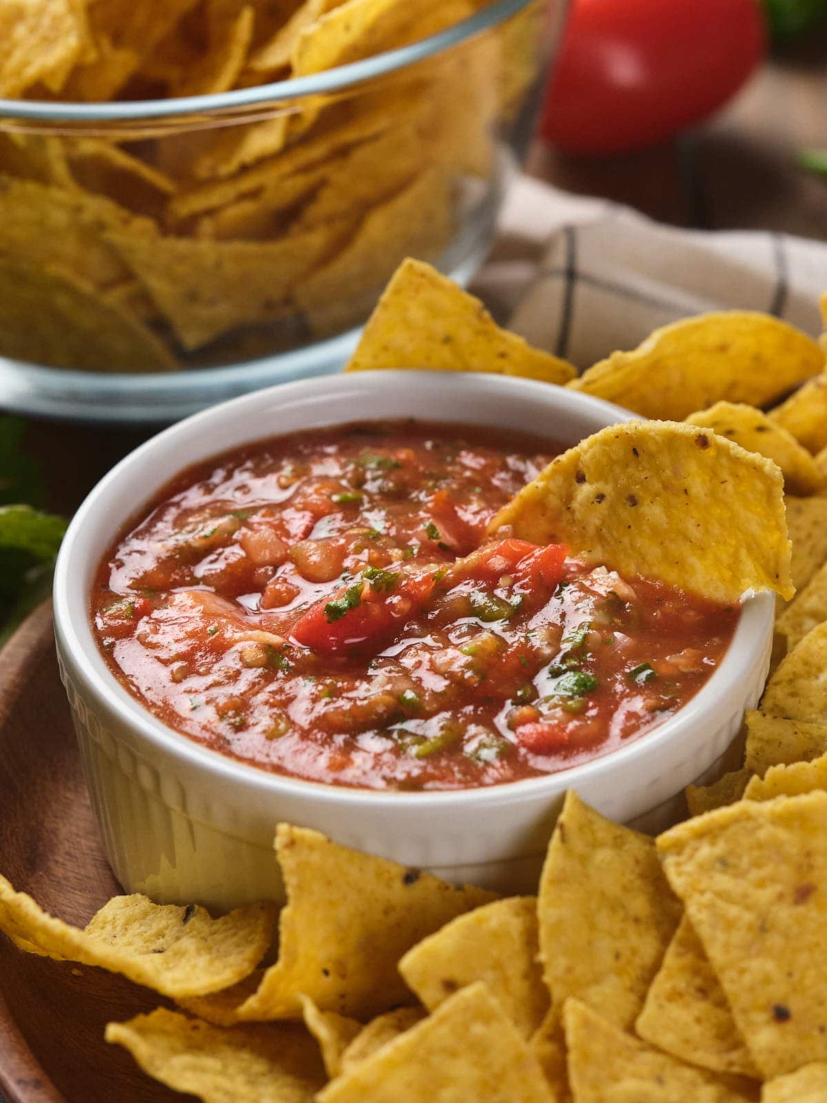 Bowl of salsa with tortilla chips surrounding it on a wooden platter.