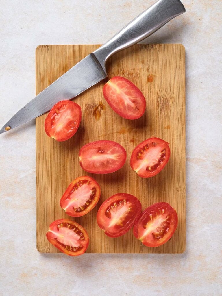 Halved tomatoes arranged on a wooden cutting board with a knife.