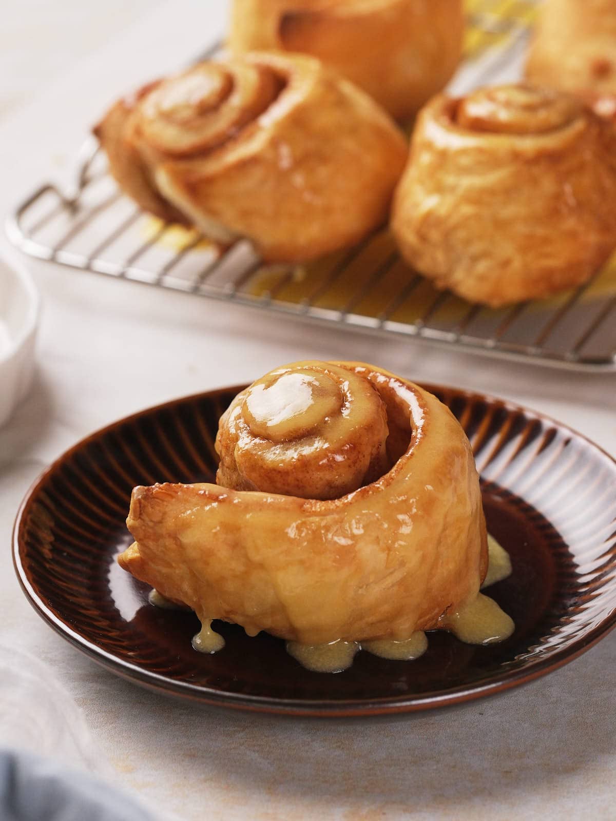 Close-up of a glazed puff pastry cinnamon roll on a brown plate.