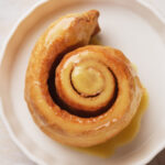 Puff pastry cinnamon roll on a white plate, viewed from above.