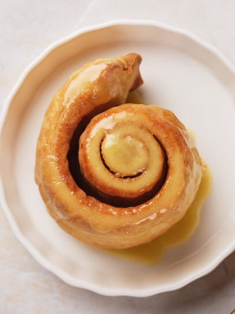 Puff pastry cinnamon roll on a white plate, viewed from above.