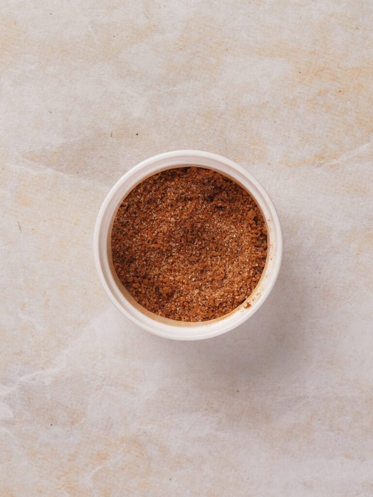 A small container filled with coarse brown seasoning on a light textured surface.