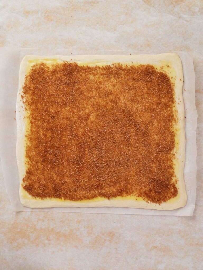 Sheet of pastry dough topped with cinnamon and sugar on parchment paper.