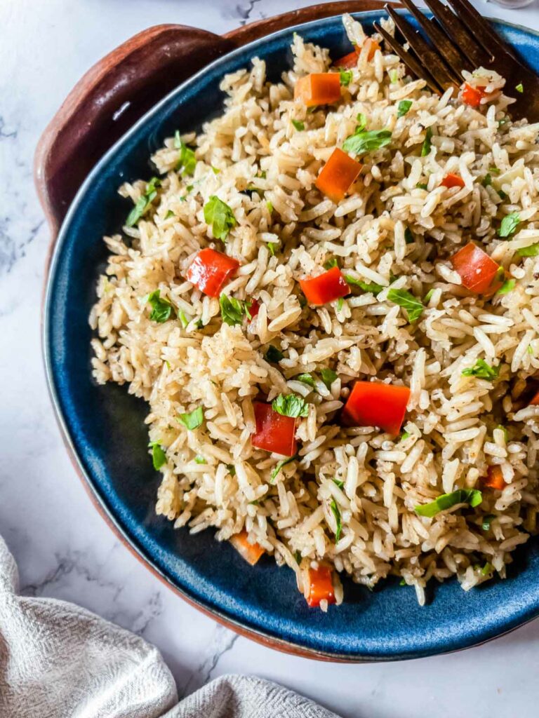 A bowl of rice pilaf with chopped red bell peppers and green herbs, with a fork on the side.