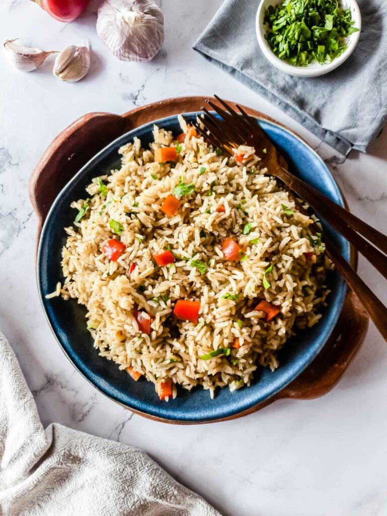 A plate of rice pilaf with red peppers and herbs, served with a fork and spoon.