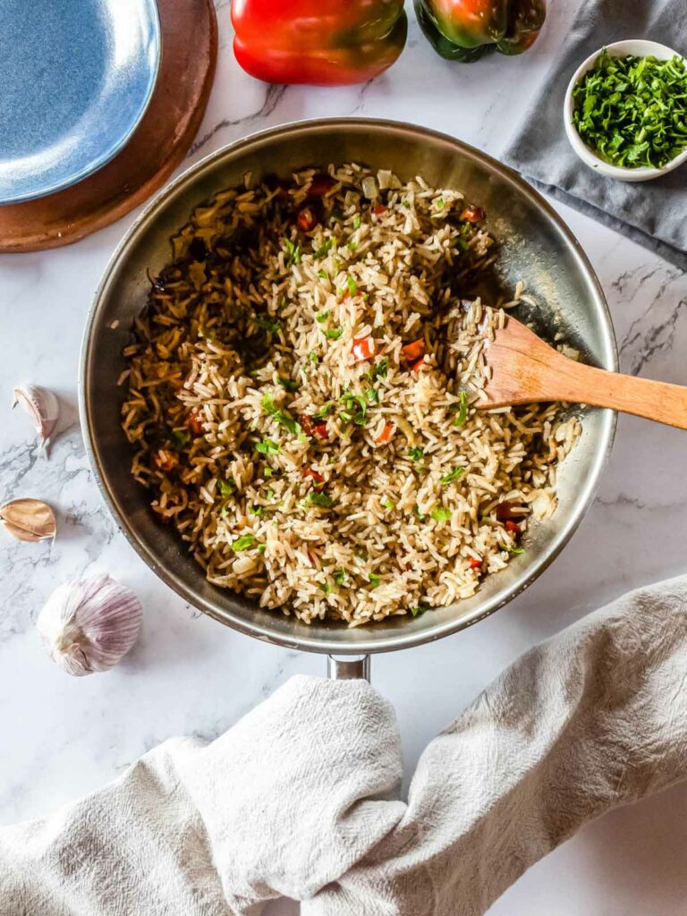 A pan of rice pilaf mixed with vegetables, including bell peppers and herbs, sits on a marble counter.