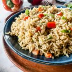 A plate of rice pilaf mixed with red bell pepper pieces and garnished with herbs.