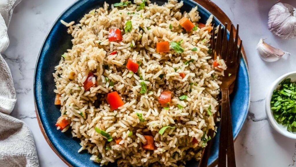 A plate of rice pilaf mixed with chopped red bell peppers and green herbs, served with a fork.