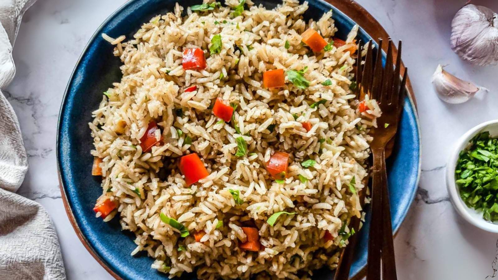 A plate of rice pilaf mixed with chopped red bell peppers and green herbs, served with a fork.