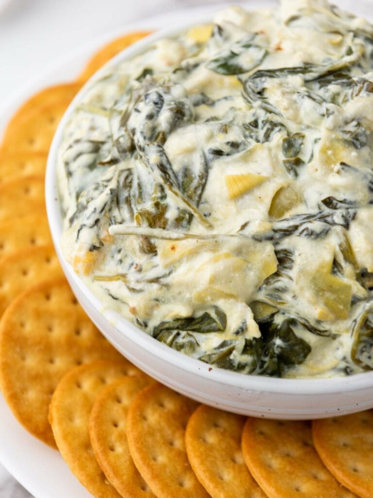 A bowl of creamy spinach and artichoke dip surrounded by round crackers.