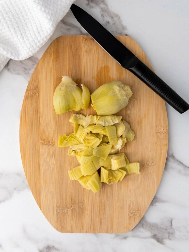 Chopped artichoke hearts on a wooden cutting board with a knife placed beside them.