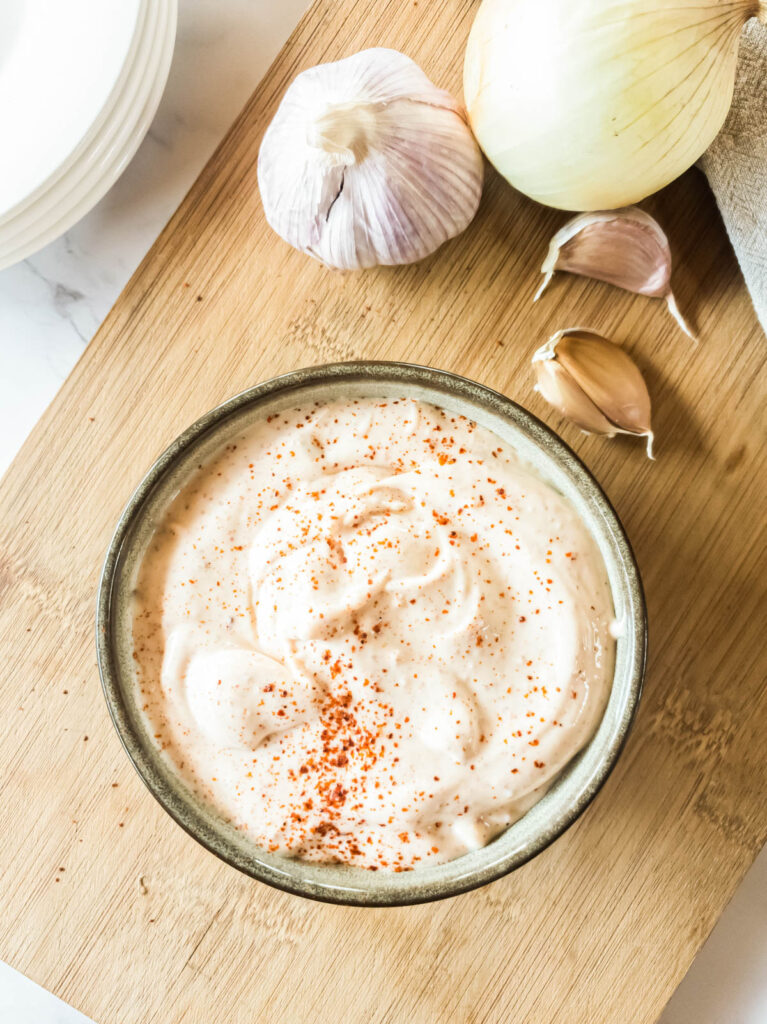 A bowl of mayonnaise sprinkled with red seasoning on a wooden board.