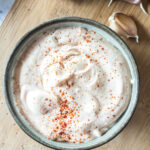 A bowl of mayonnaise topped with paprika on a wooden surface.