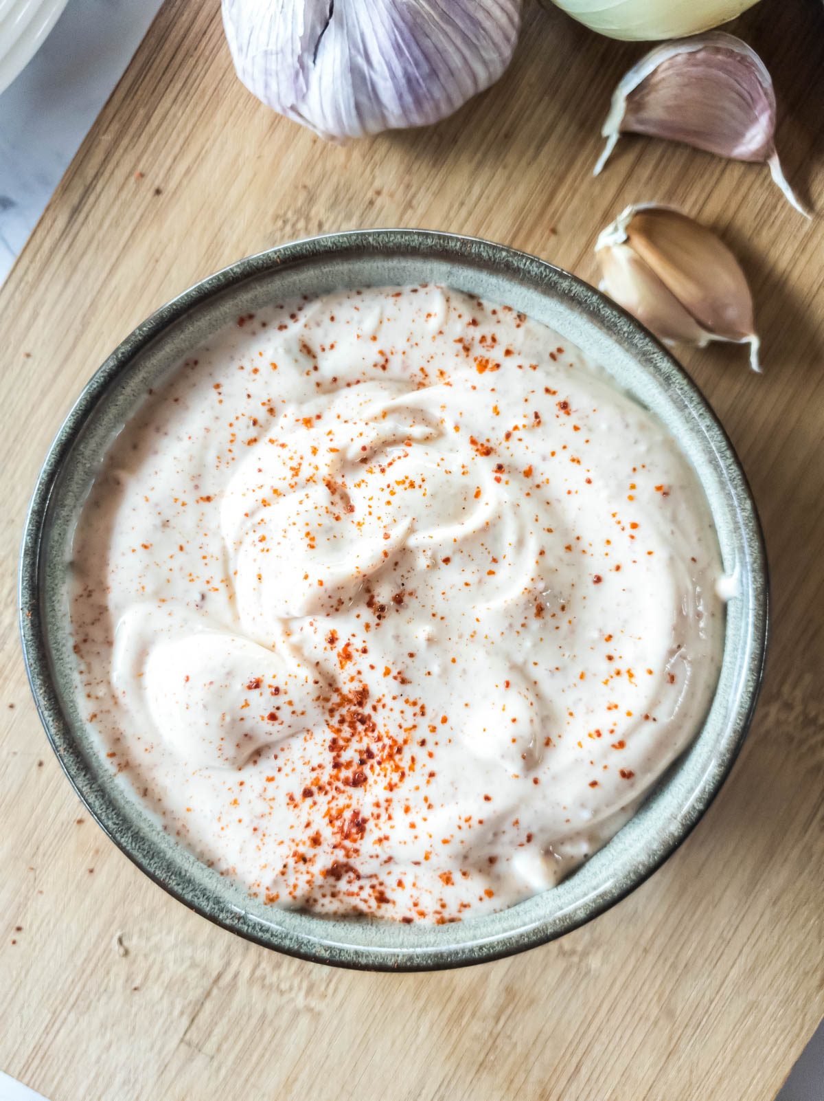 A bowl of mayonnaise topped with paprika on a wooden surface.