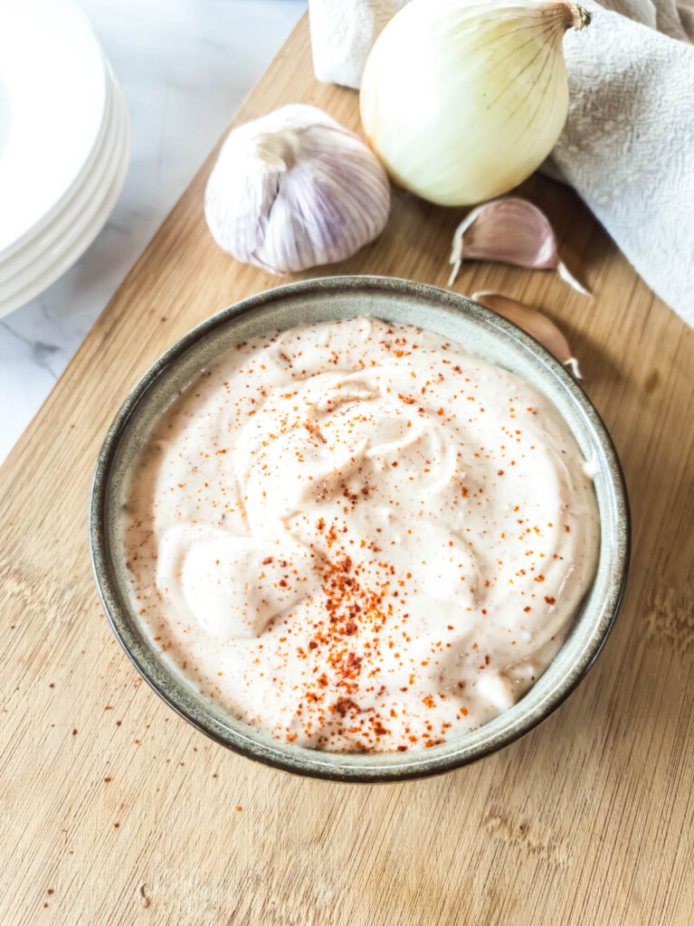 A bowl of mayonnaise sprinkled with paprika, placed on a wooden surface.