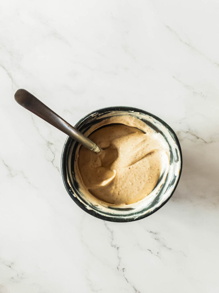 A bowl of creamy tan sauce with a spoon, placed on a marble surface.